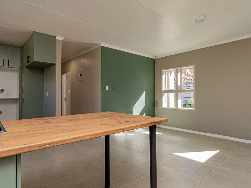 An open-plan living and kitchen area featuring tiled floors, built-in cabinetry with a hob, and direct access to the exterior.