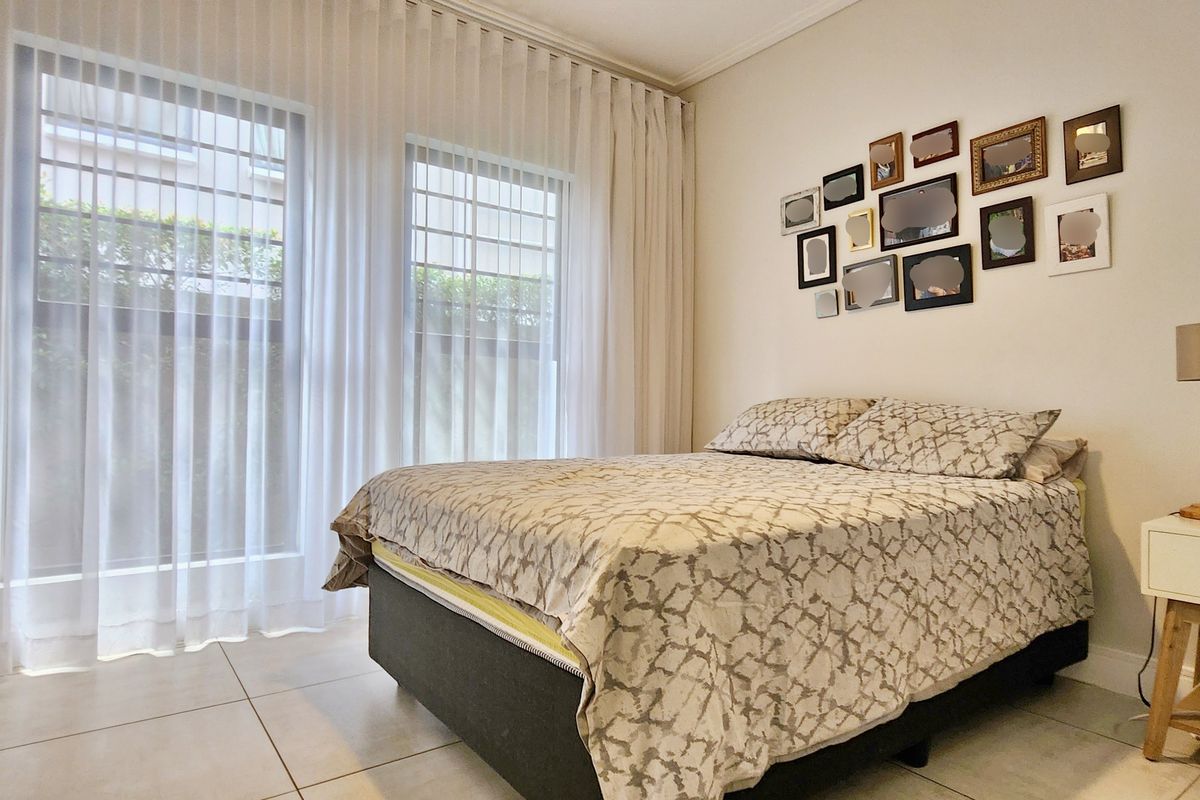 A well-lit bedroom featuring neutral tiled flooring and large windows with floor-to-ceiling curtains, creating a bright and comfortable living space.