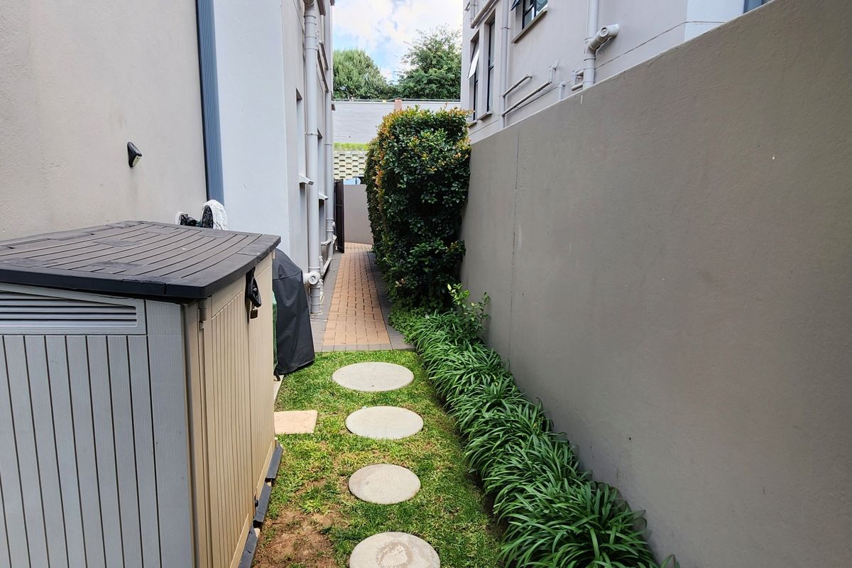 A narrow side passage featuring a paved walkway, stepping stones, and a landscaped garden bed bordered by a high boundary wall.