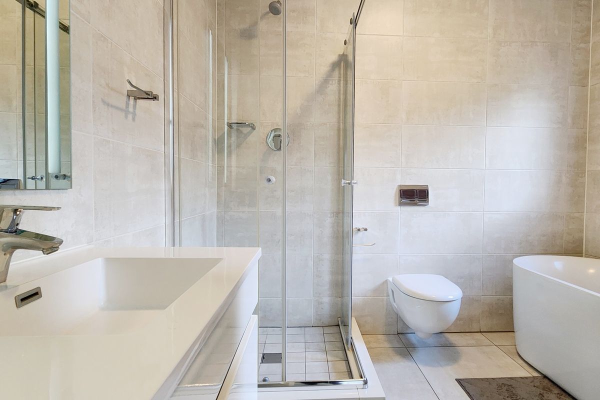 Modern bathroom featuring a sleek freestanding bathtub, a glass-enclosed shower, a wall-mounted toilet, and a contemporary vanity basin with neutral tiling.