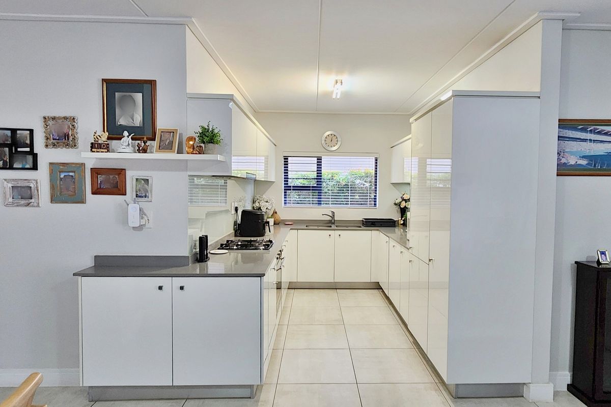 A modern, U-shaped kitchen featuring white cabinetry, stone countertops, a gas hob, and tiled flooring, offering a clean and functional workspace.