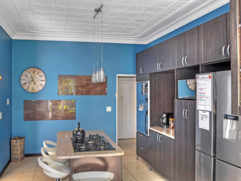 Modern kitchen featuring dark cabinetry, granite countertops, a central island with a gas cooktop, and a decorative pressed metal ceiling.