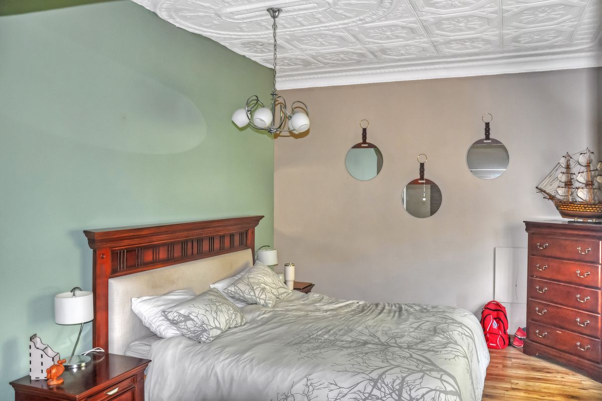 A bedroom featuring a decorative pressed metal ceiling, hardwood flooring, and a dual-tone wall finish.