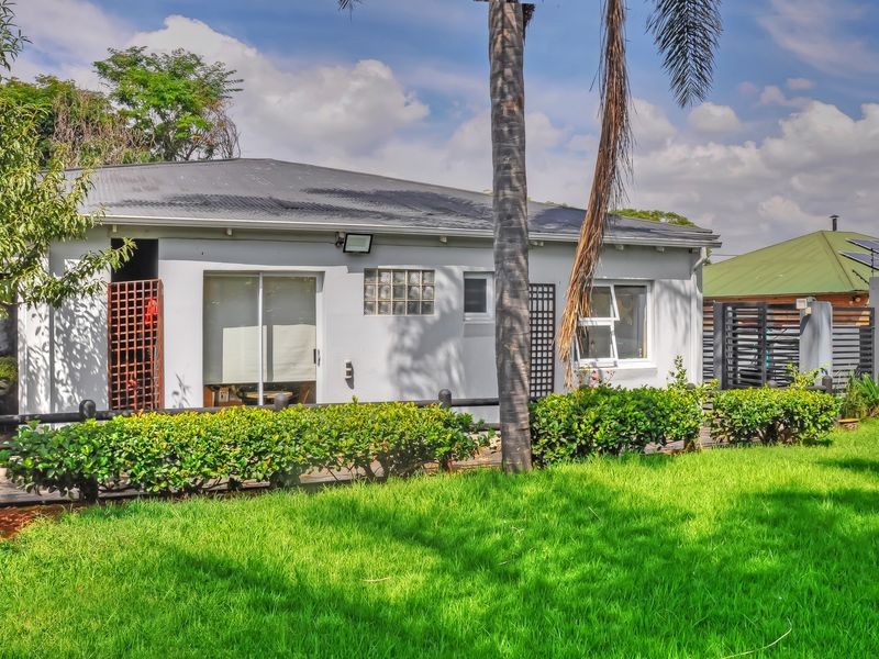 Rear view of the property featuring a corrugated metal roof, sliding glass doors, and a well-maintained lawn with established hedging.