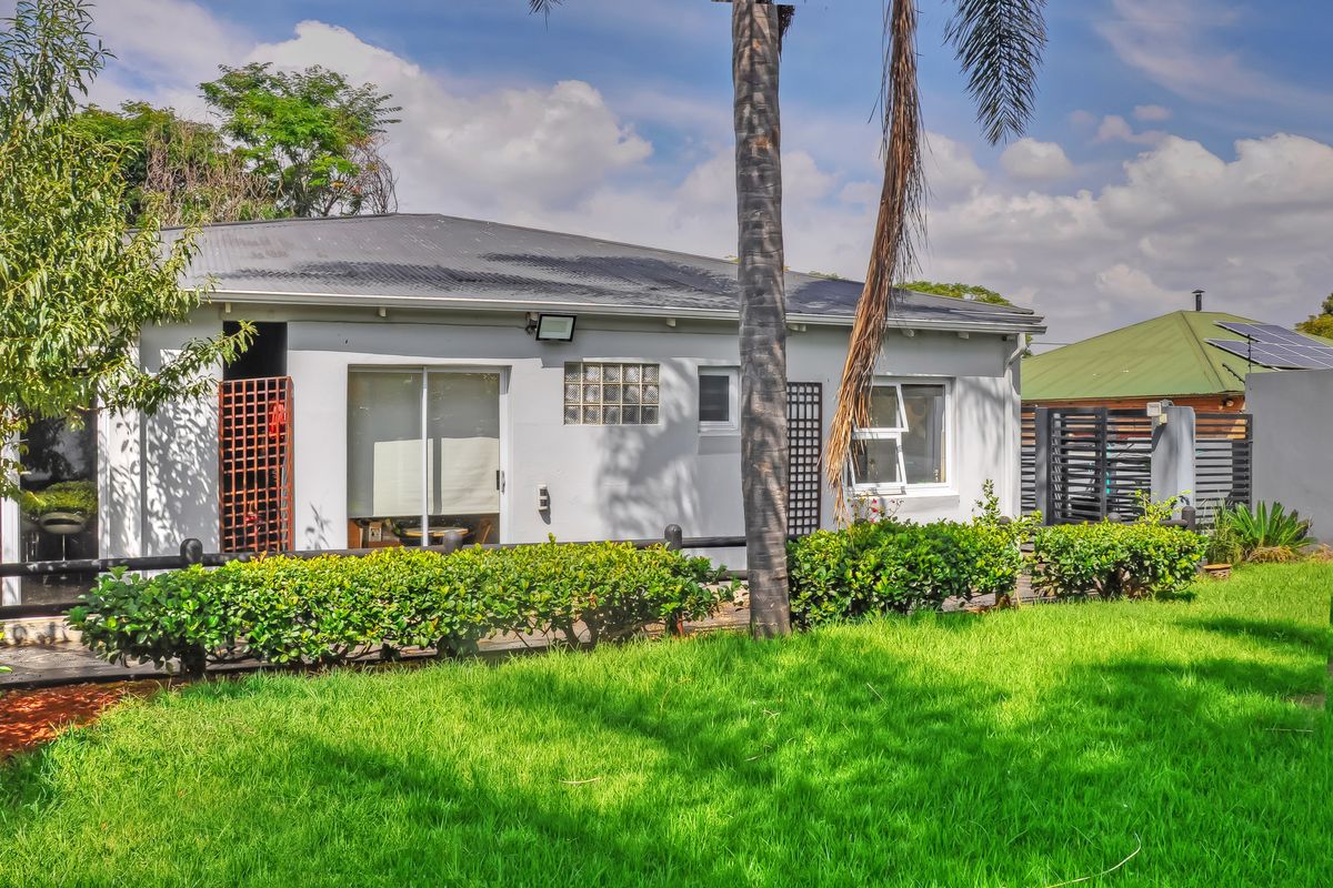 Rear view of the property featuring a corrugated metal roof, sliding glass doors, and a well-maintained lawn with established hedging.