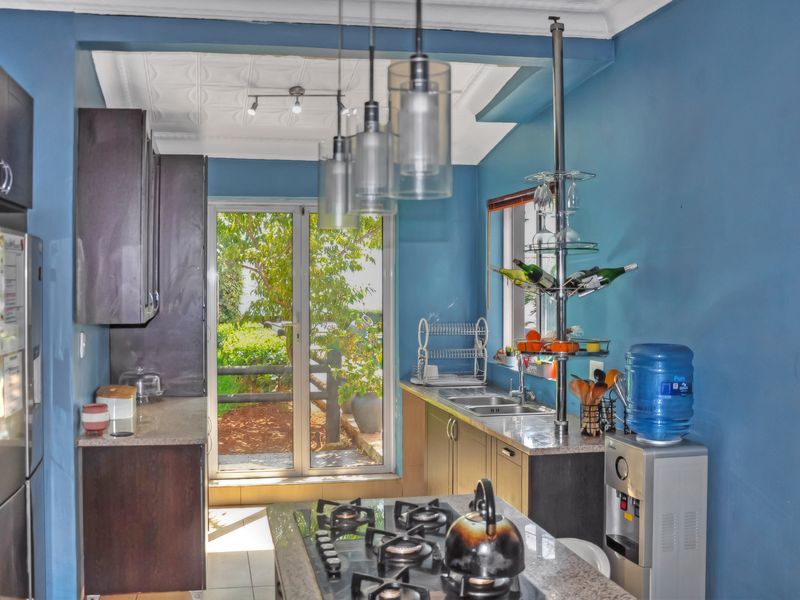 A functional kitchen featuring dark cabinetry, granite countertops, a central gas cooktop, and direct access to the garden through a sliding glass door.