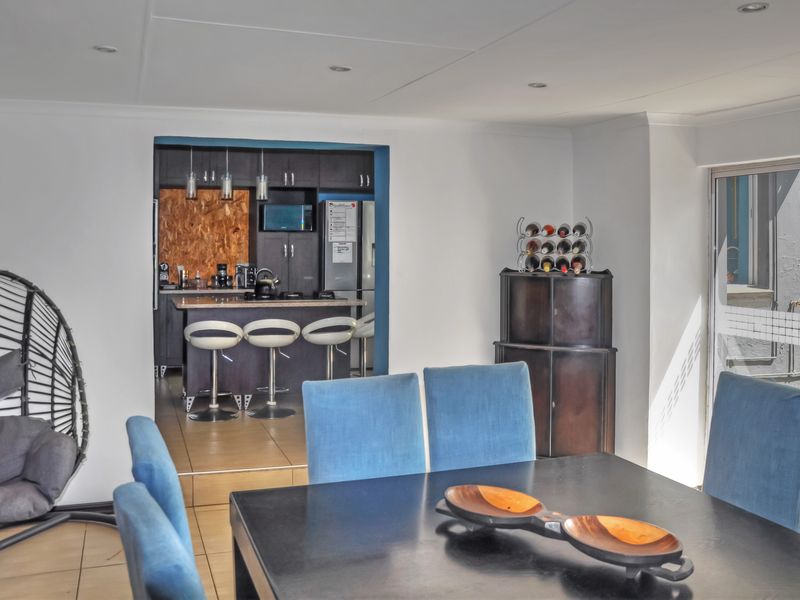 Open plan dining area flowing into a modern kitchen with dark cabinetry, a central island, and direct access to the outdoor area via sliding doors.
