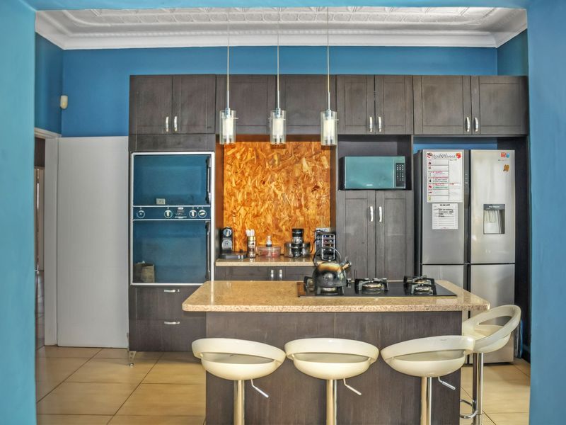 A functional kitchen featuring dark cabinetry, stone countertops, a central island with a gas cooktop, and decorative ceiling detailing.