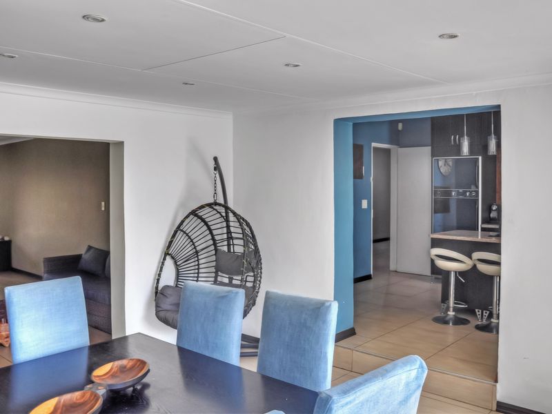 Open plan dining area leading into a kitchen with a breakfast bar, featuring tiled flooring and recessed lighting throughout the space.