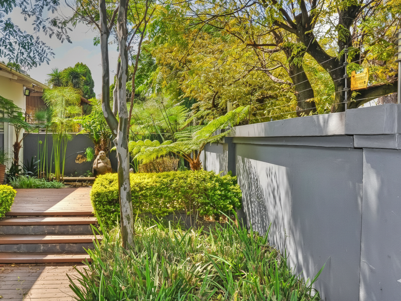 A well-maintained garden area featuring timber decking, lush landscaping, and a secure boundary wall with integrated electric fencing and lighting.