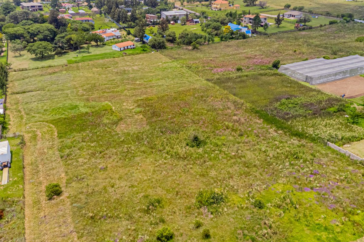 An aerial view of a large, undeveloped residential plot featuring open grassland and surrounding neighborhood infrastructure.