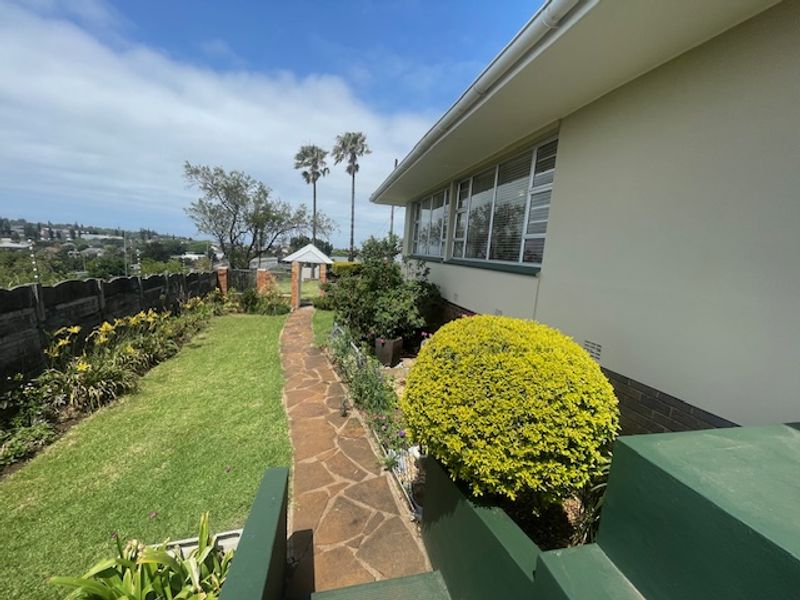 A well-maintained rear garden featuring a stone paved pathway, manicured landscaping, and a clear view of the property's exterior facade and boundary wall.
