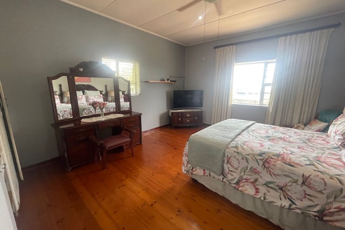 Spacious bedroom featuring polished hardwood flooring, a ceiling fan, and large windows with curtain rails, offering a comfortable and well-lit living space.