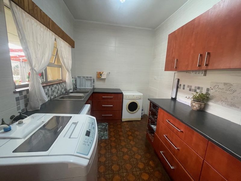 A functional laundry room featuring built-in wooden cabinetry, dark laminate countertops, a stainless steel sink, and tiled finishes.