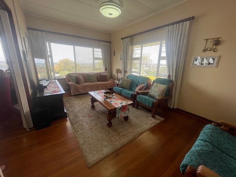 A comfortable living room featuring polished hardwood flooring, large windows providing natural light, and a classic ceiling light fixture.