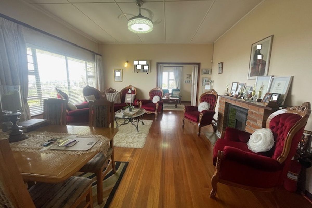 Spacious living room featuring polished hardwood flooring, a classic brick fireplace, and a ceiling fan, offering a warm and inviting atmosphere.
