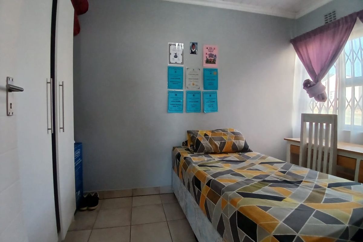 A functional bedroom featuring tiled flooring, a built-in wardrobe, and a window with security gate, providing a practical living space.