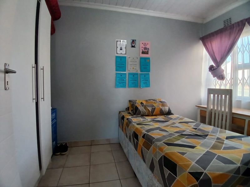 A functional bedroom featuring tiled flooring, a built-in wardrobe, and a window with security gate, providing a practical living space.