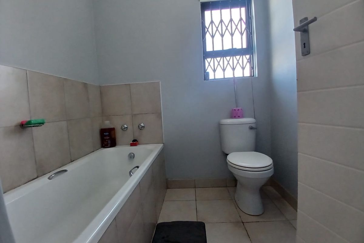 A functional bathroom featuring a standard bathtub, toilet, and neutral wall and floor tiling with a security-fitted window.