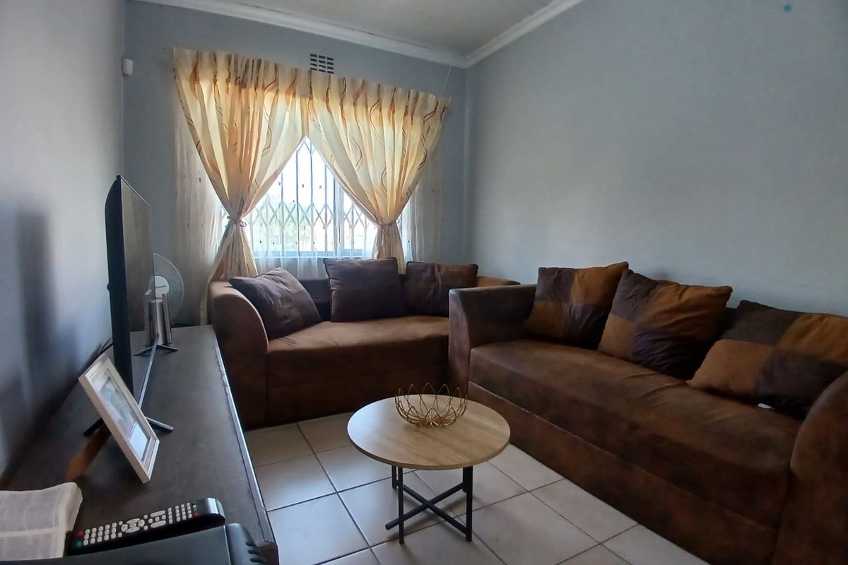 A functional living room featuring tiled flooring, neutral wall finishes, and a window fitted with security bars.