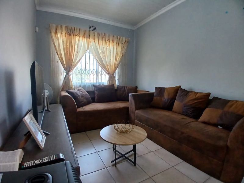 A functional living room featuring tiled flooring, neutral wall finishes, and a window fitted with security bars.