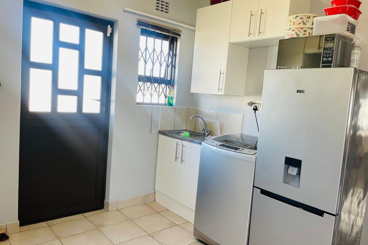 Functional laundry area featuring built-in cabinetry, a stainless steel sink, tiled splashback, and direct access to the exterior via a secure door.