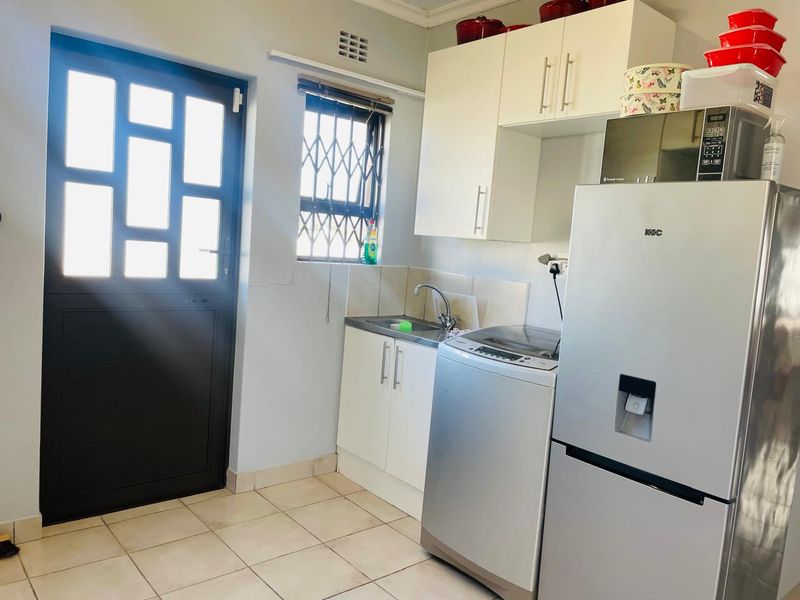 Functional laundry area featuring built-in cabinetry, a stainless steel sink, tiled splashback, and direct access to the exterior via a secure door.