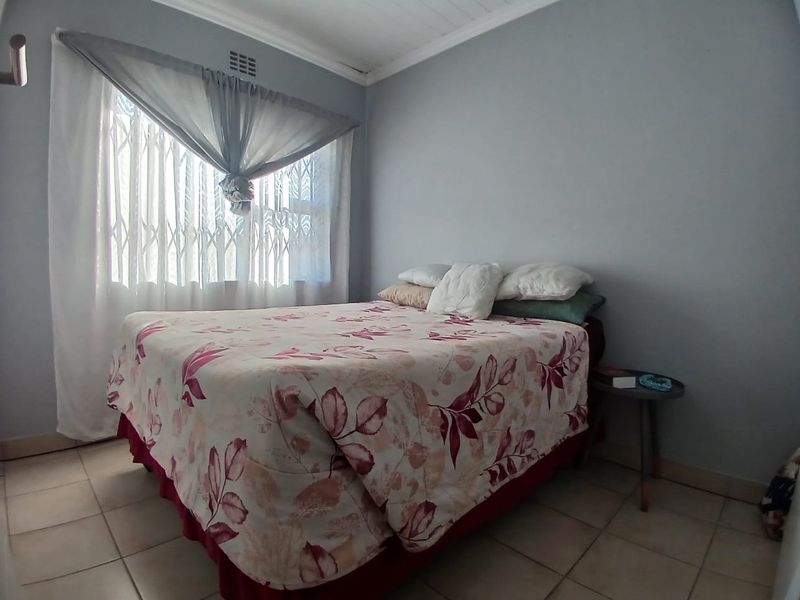 A functional bedroom featuring tiled flooring, a security gate on the window, and a ceiling vent.