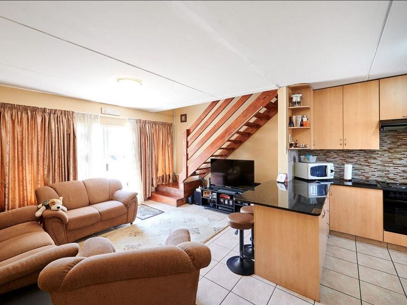 Open-plan living area featuring a kitchen with granite countertops, built-in appliances, and a wooden staircase leading to the upper level.