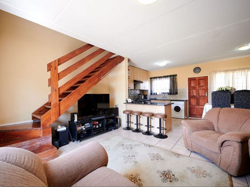 Open-plan living area featuring a wooden staircase, tiled flooring, and a functional kitchen with granite countertops and built-in cabinetry.