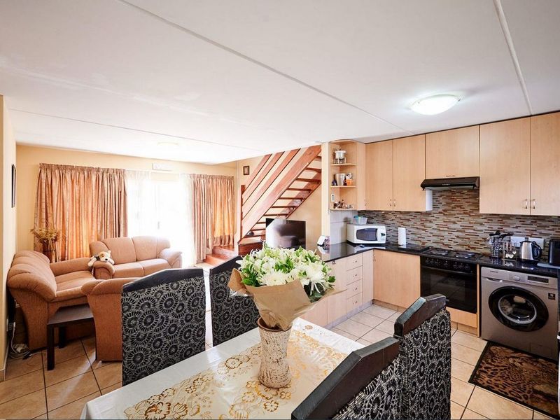 Open-plan living and dining area featuring a functional kitchen with built-in cabinetry, granite countertops, and a staircase leading to the upper level.