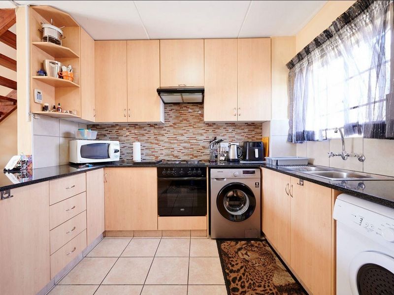 Functional kitchen featuring light wood cabinetry, granite countertops, mosaic backsplash, built-in oven, hob, extractor fan, and integrated laundry plumbing.