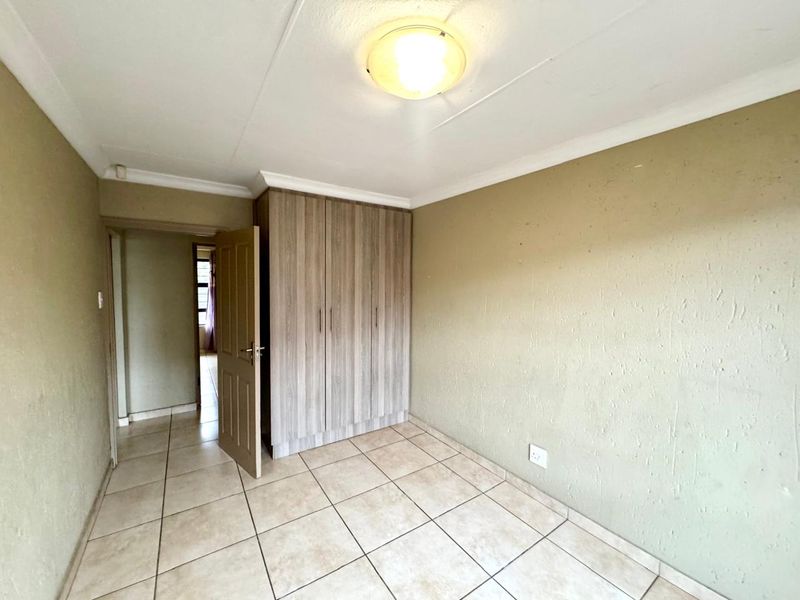 An empty bedroom featuring tiled flooring, a built-in wardrobe, and neutral wall finishes, offering a blank canvas for personalization.