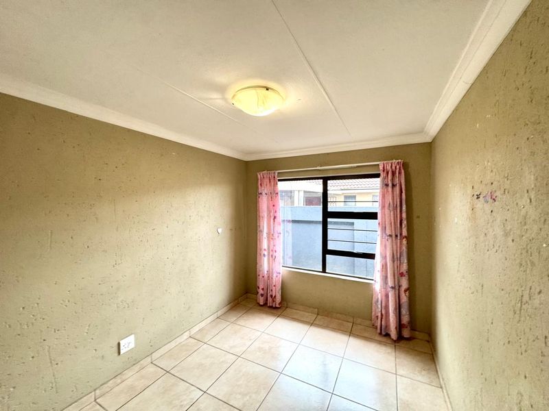 An empty bedroom featuring tiled flooring, a ceiling light fixture, and a window fitted with security bars.