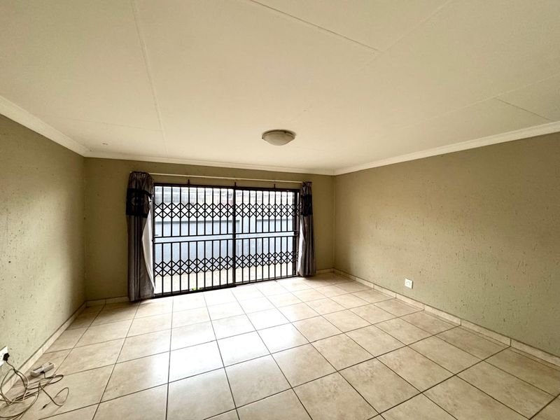 An empty living room featuring ceramic floor tiles, a sliding door with a security gate, and neutral wall finishes requiring minor cosmetic attention.