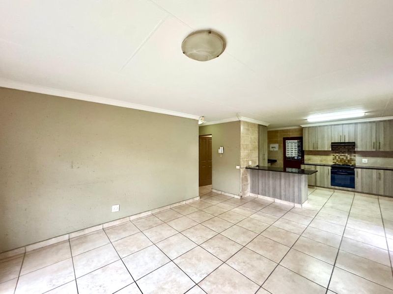 Open-plan living and kitchen area featuring tiled flooring, a breakfast bar, and built-in cabinetry with integrated cooking appliances.