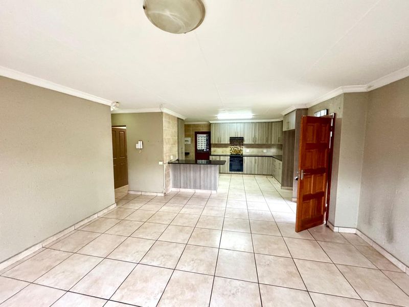 Spacious open-plan living and kitchen area featuring tiled flooring, built-in cabinetry, and a breakfast counter, offering a versatile layout for modern living.