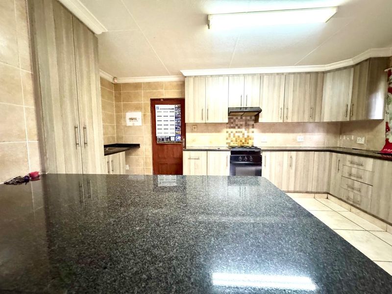 A functional kitchen featuring granite countertops, ample built-in cabinetry, a built-in oven with extractor fan, and tiled flooring throughout.