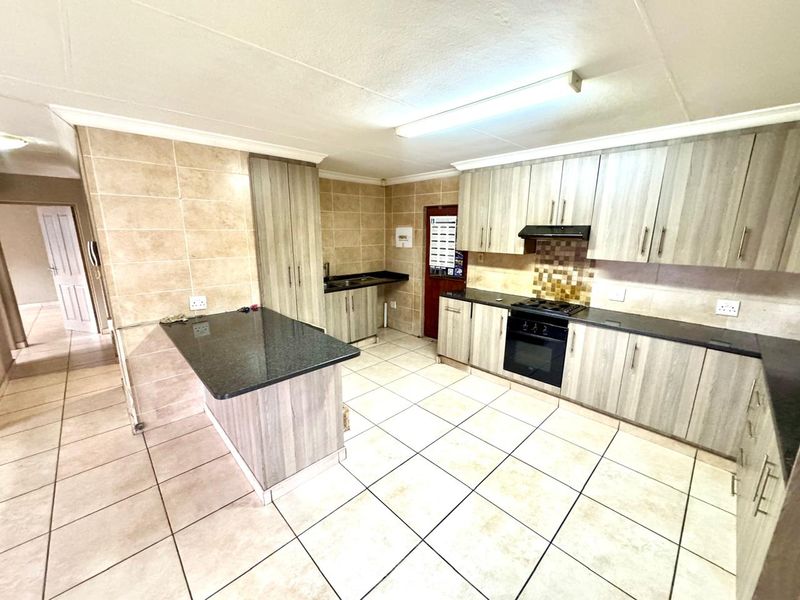 A spacious kitchen featuring light wood-grain cabinetry, granite countertops, a built-in oven with gas hob, and neutral tiled flooring throughout.
