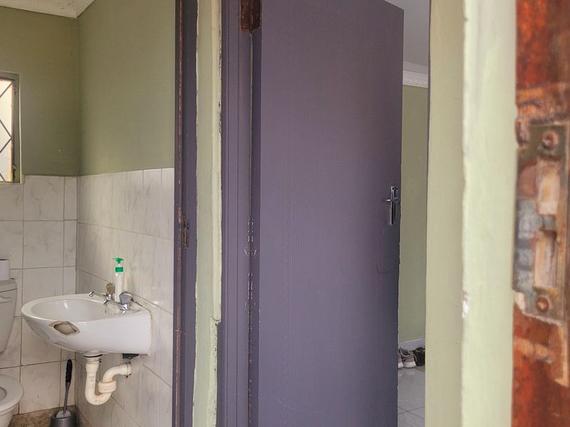 A compact bathroom featuring a pedestal washbasin and toilet, with tiled splashbacks and a diamond-pattern window. The space requires cosmetic updates.