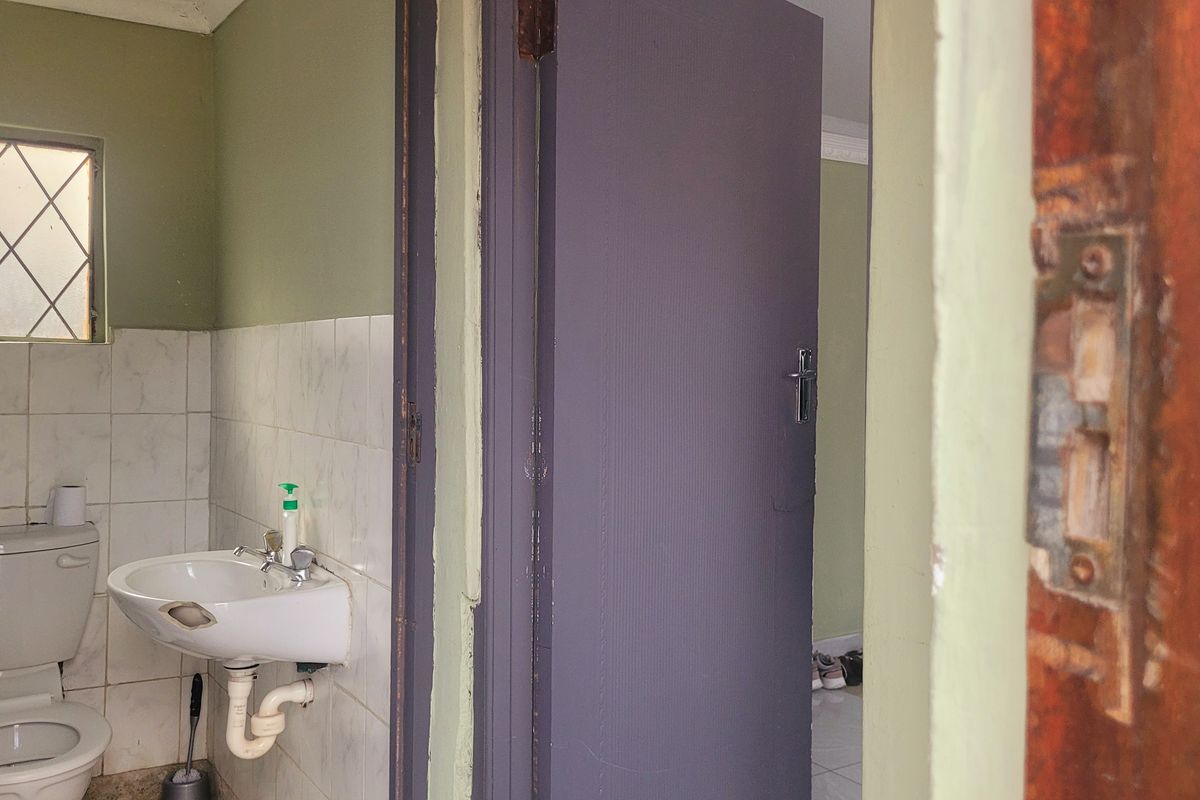 A compact bathroom featuring a pedestal washbasin and toilet, with tiled splashbacks and a diamond-pattern window. The space requires cosmetic updates.