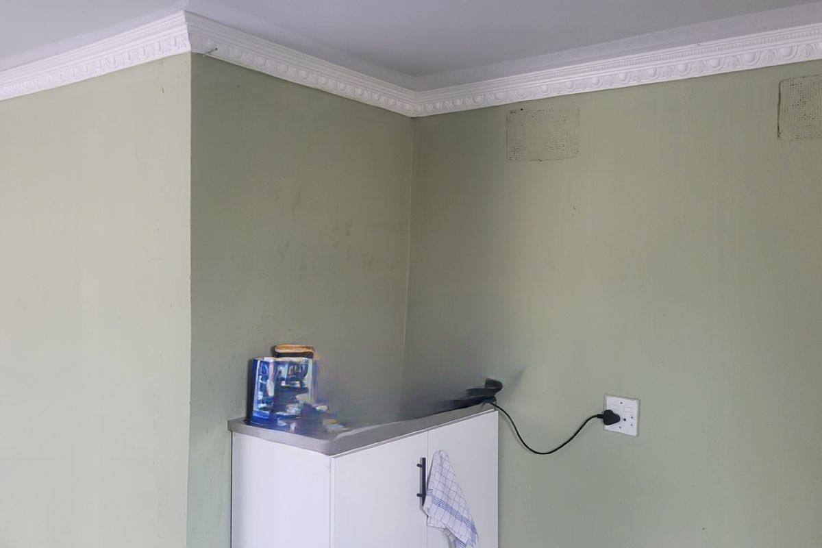 A corner view of a kitchen area featuring built-in cabinetry, decorative crown molding, and wall-mounted electrical points.