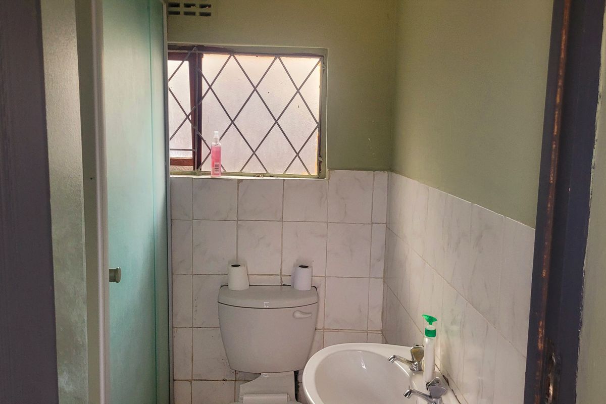 A compact bathroom featuring a standard toilet, pedestal basin, and tiled splashback, with security bars on the window.