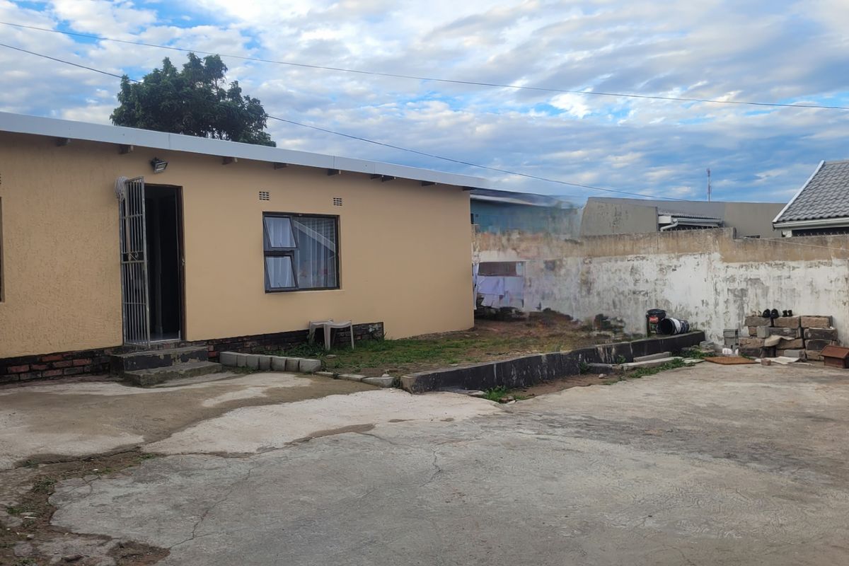Rear exterior view of the property featuring a concrete courtyard, boundary wall, and access to the main building via a security gate.