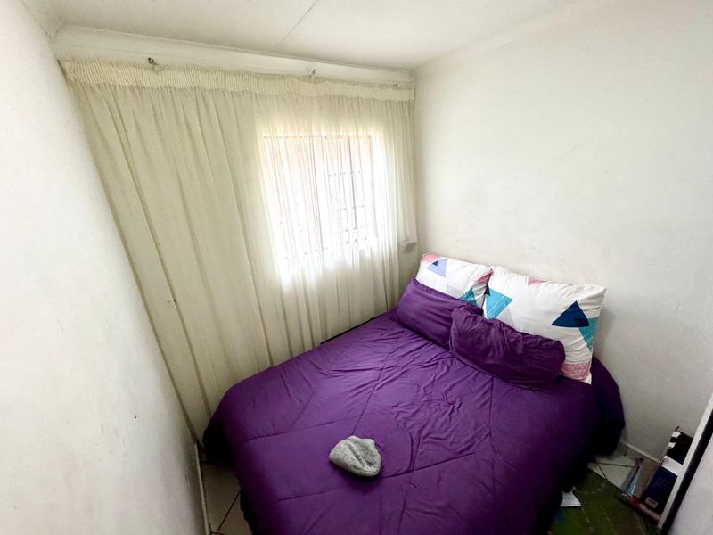 A compact bedroom featuring tiled flooring and a window with installed curtain rails, providing a functional sleeping space.