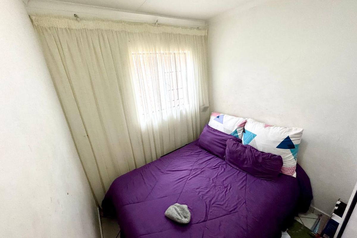 A compact bedroom featuring tiled flooring and a window with installed curtain rails, providing a functional sleeping space.
