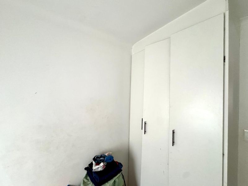 A bedroom corner featuring white built-in cupboards with modern handles, requiring minor cosmetic wall touch-ups.