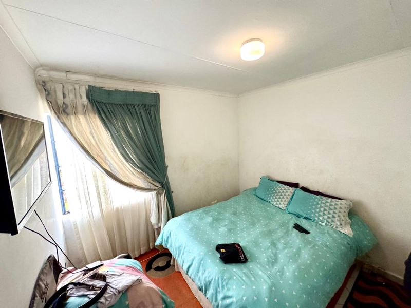 A compact bedroom featuring a window with curtain rails and a central ceiling light fixture, requiring cosmetic updates to the wall finishes.