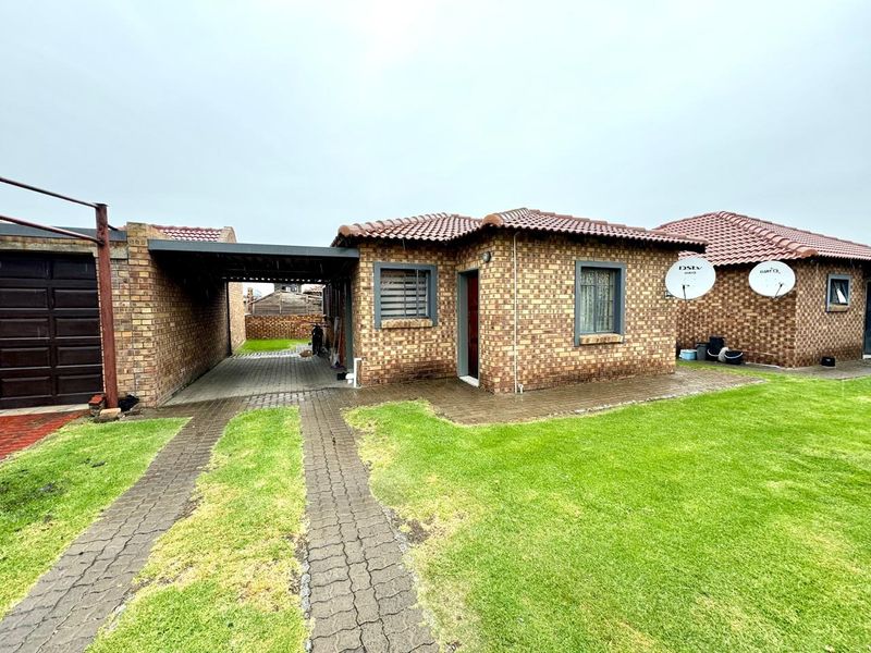 Front view of a face brick townhouse featuring a tiled roof, a covered carport, and a well-maintained lawn area.