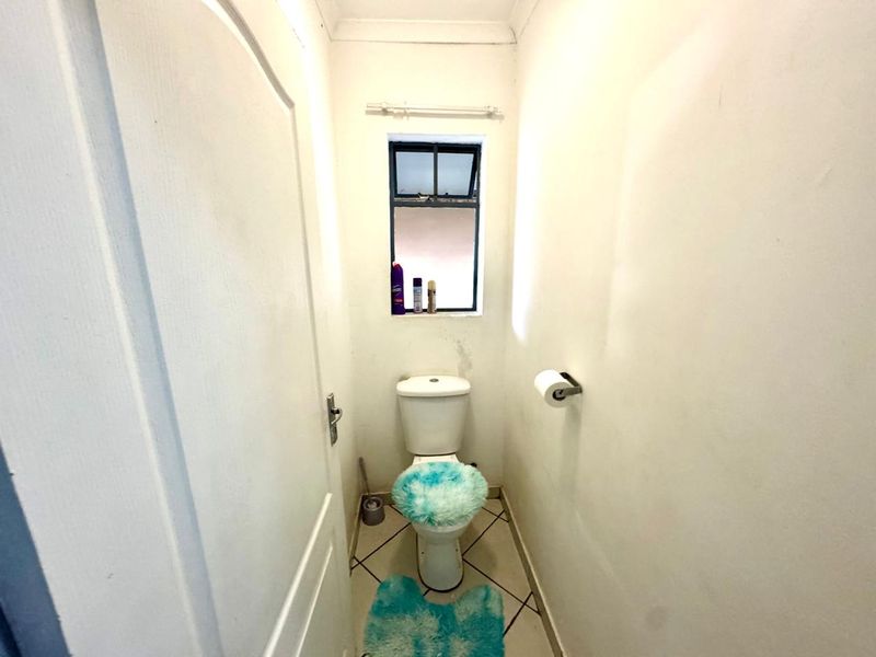 A compact guest toilet featuring tiled flooring and a small window, showing signs of wear and requiring minor cosmetic attention.